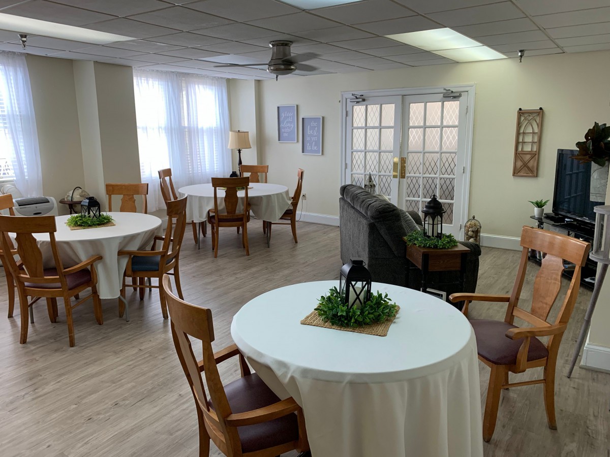 A cozy dining room with round tables and wooden chairs, decorated with small potted plants, illuminated by natural light.