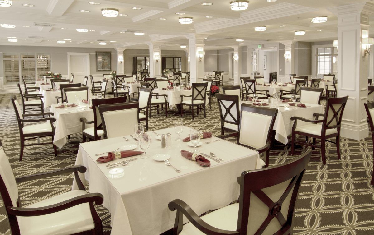 An elegant restaurant dining room with neatly arranged tables and chairs, featuring white tablecloths and a formal setting.