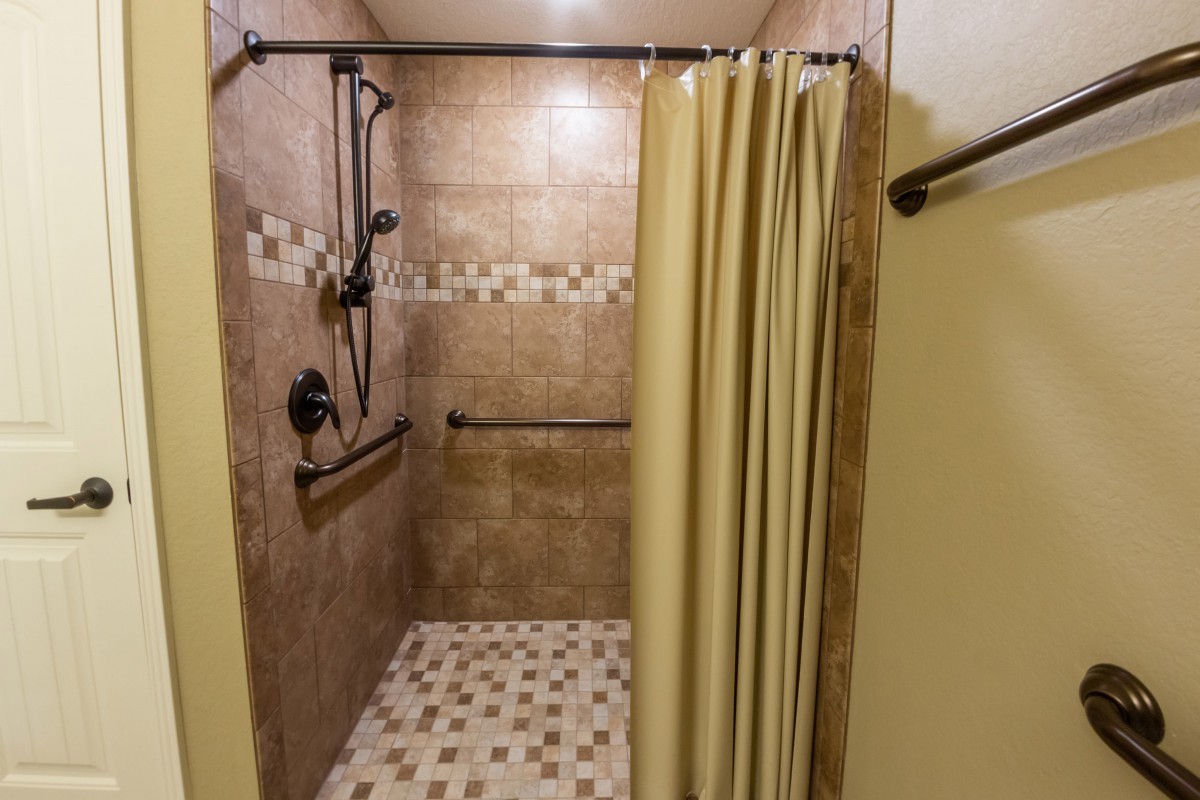 A bathroom shower with tiled walls and a shower curtain, featuring a handrail for accessibility.