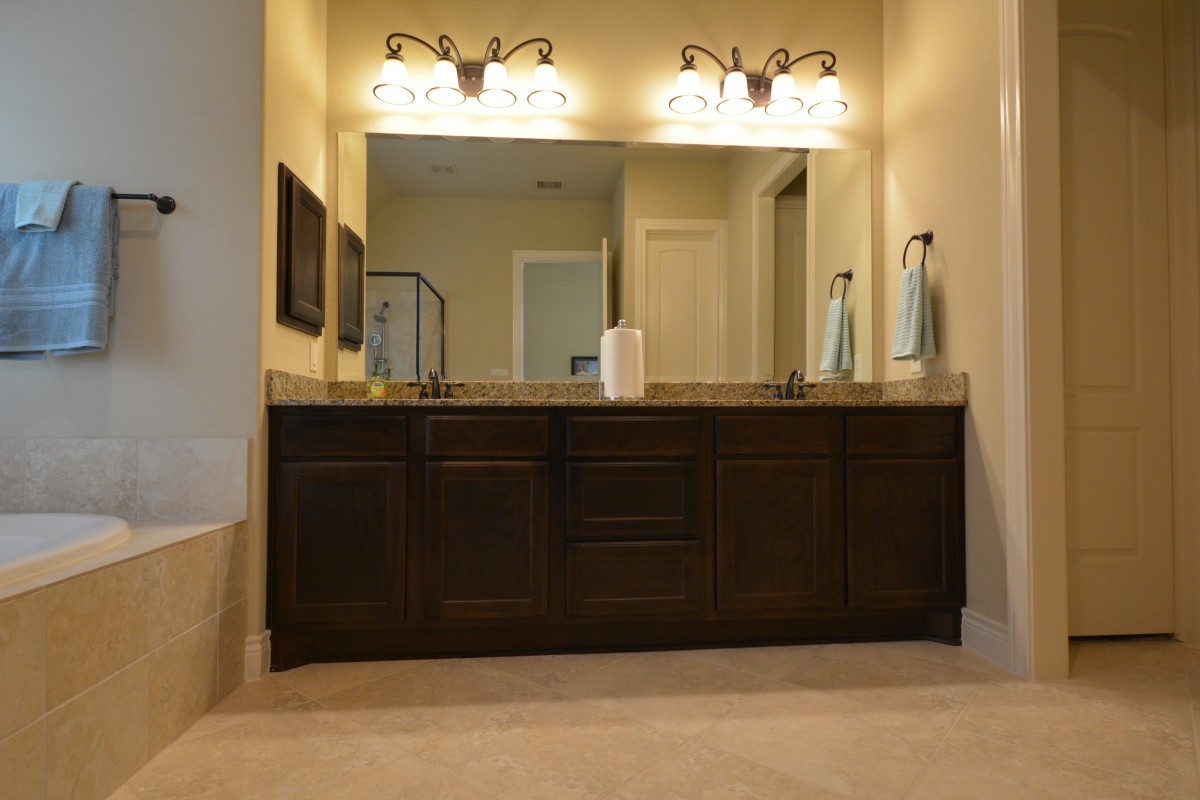 A spacious bathroom featuring a large mirror, double sink vanity, and elegant lighting fixtures.