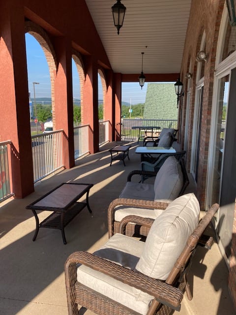 A sunny balcony with comfortable outdoor seating and tables.
