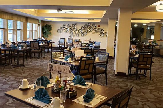 A well-arranged dining area with neatly set tables, featuring blue napkins and an artistic wall decoration.
