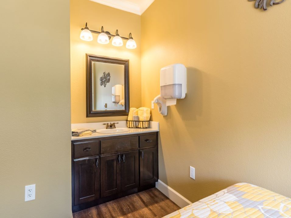 A bathroom with a dark wood cabinet, large mirror, and bright lighting against yellow walls.