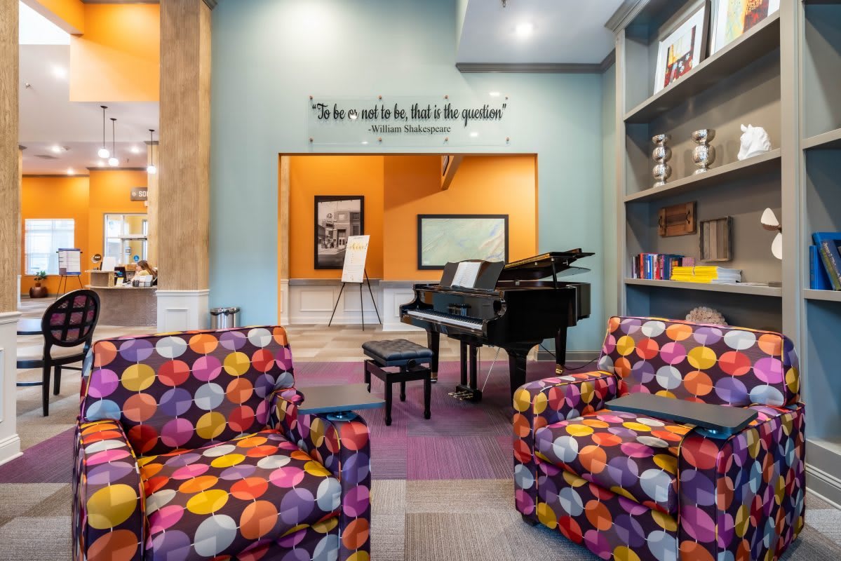 A vibrant music room featuring a grand piano, colorful chairs, and an inspirational quote on the wall.