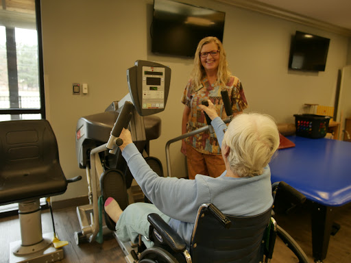 A healthcare professional assists an elderly patient using exercise equipment during a rehabilitation session.