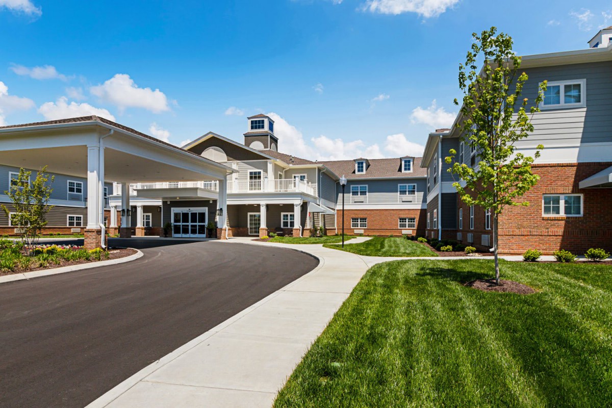 A modern residential building with a driveway and landscaped surroundings under a clear blue sky.