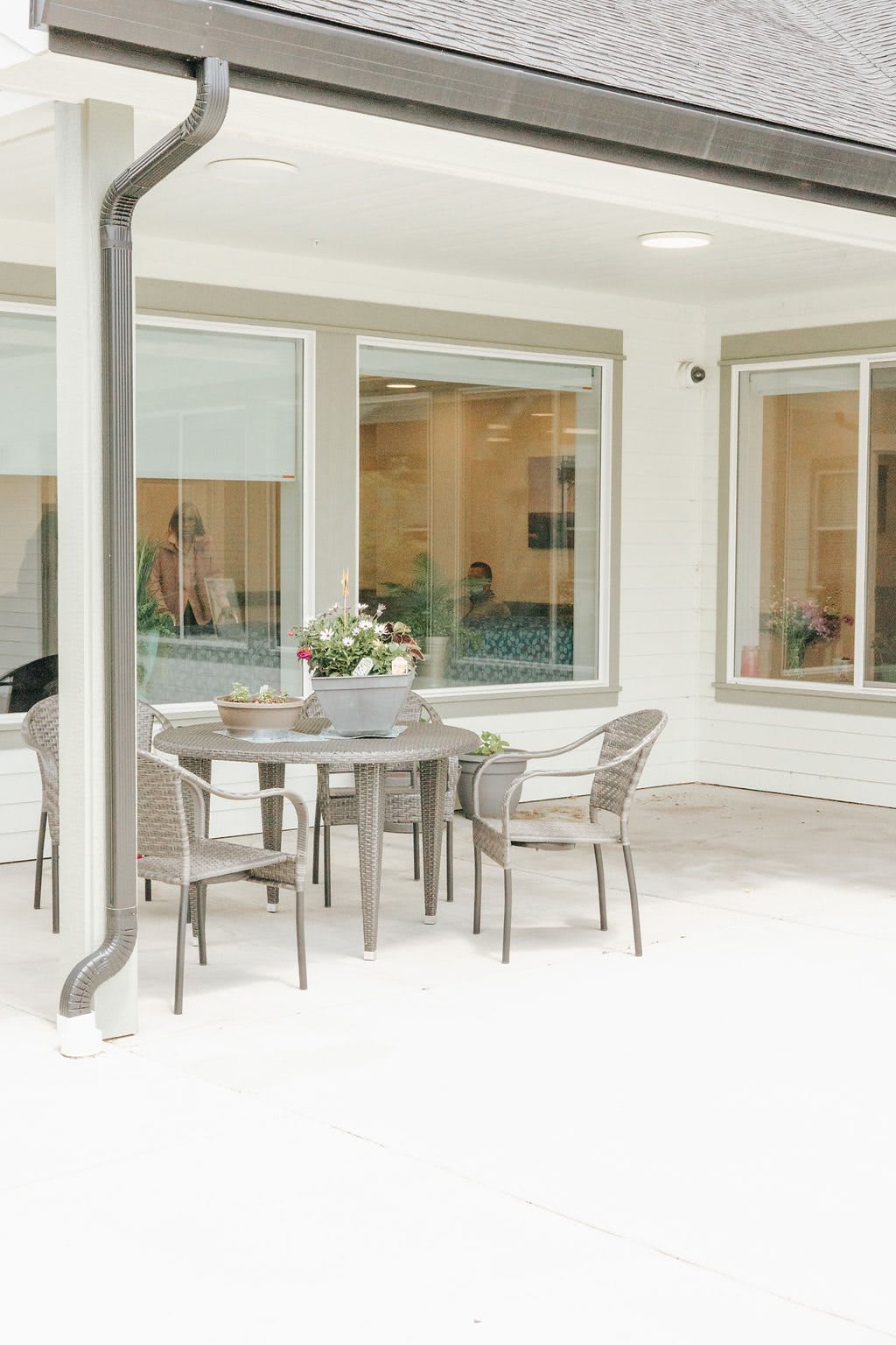 A minimalist patio with a round table surrounded by chairs, set against large windows.