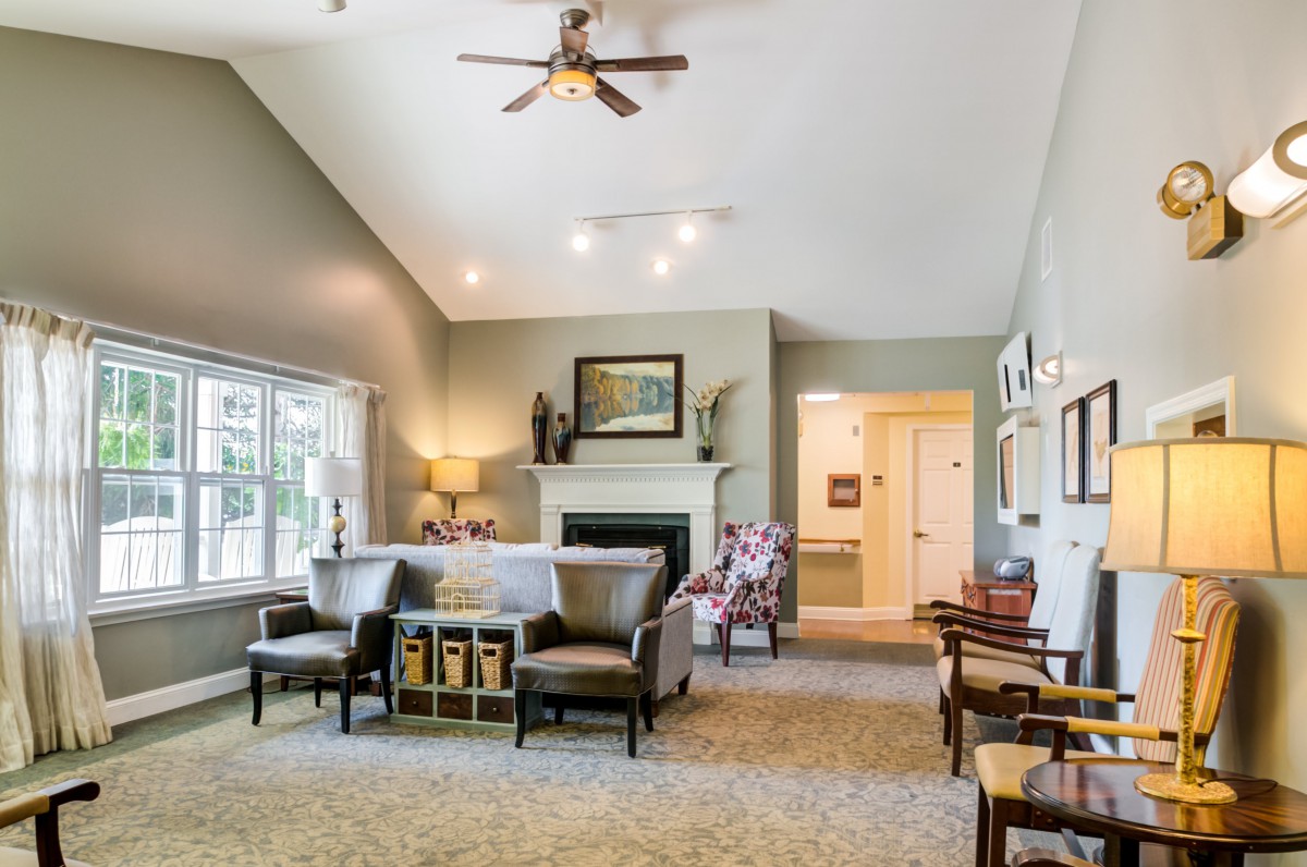 A cozy living room with a high ceiling, featuring a sofa and chairs around a fireplace.
