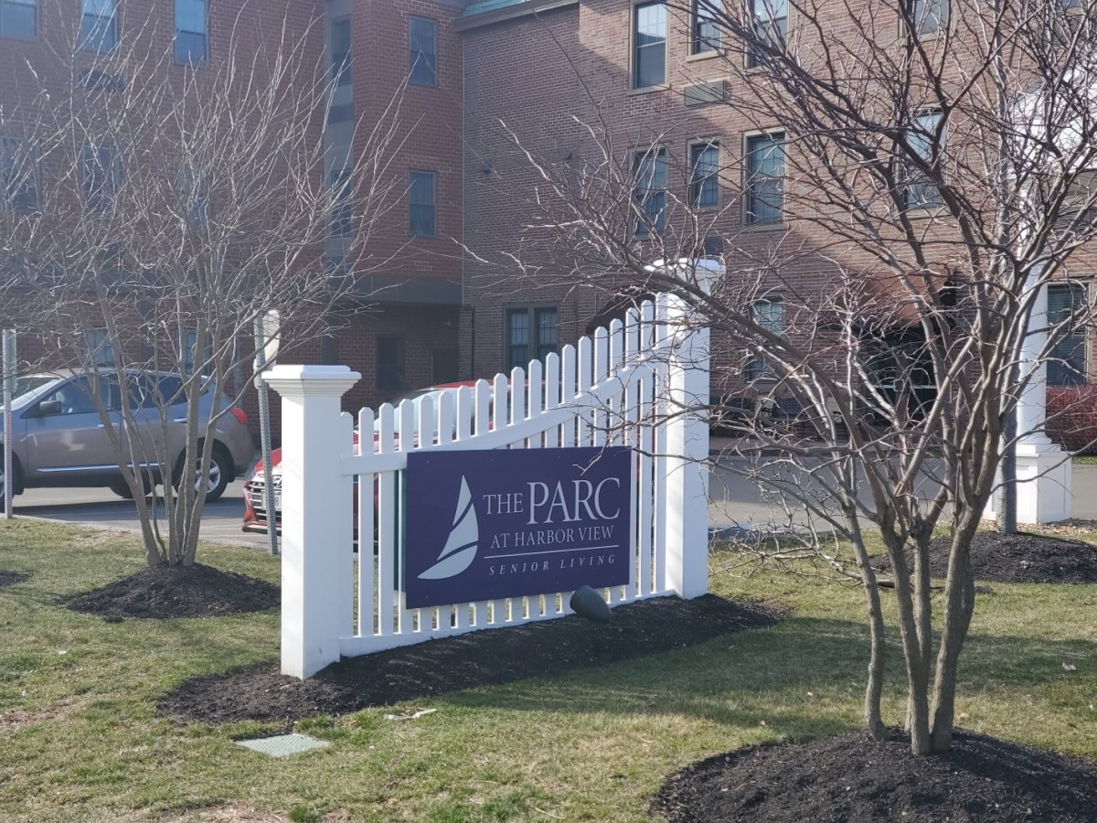 A sign for 'The Parc at Harbor View' situated in front of a building, surrounded by trees and grass.