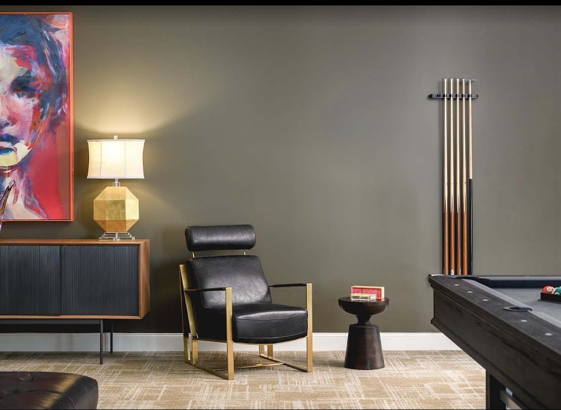 A modern living room with sleek furniture and minimalist decor, featuring a comfortable armchair, a vintage lamp, and a pool table.