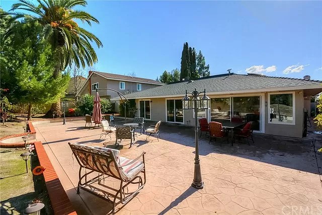 A spacious backyard patio with outdoor furniture and a palm tree under a clear, sunny sky.
