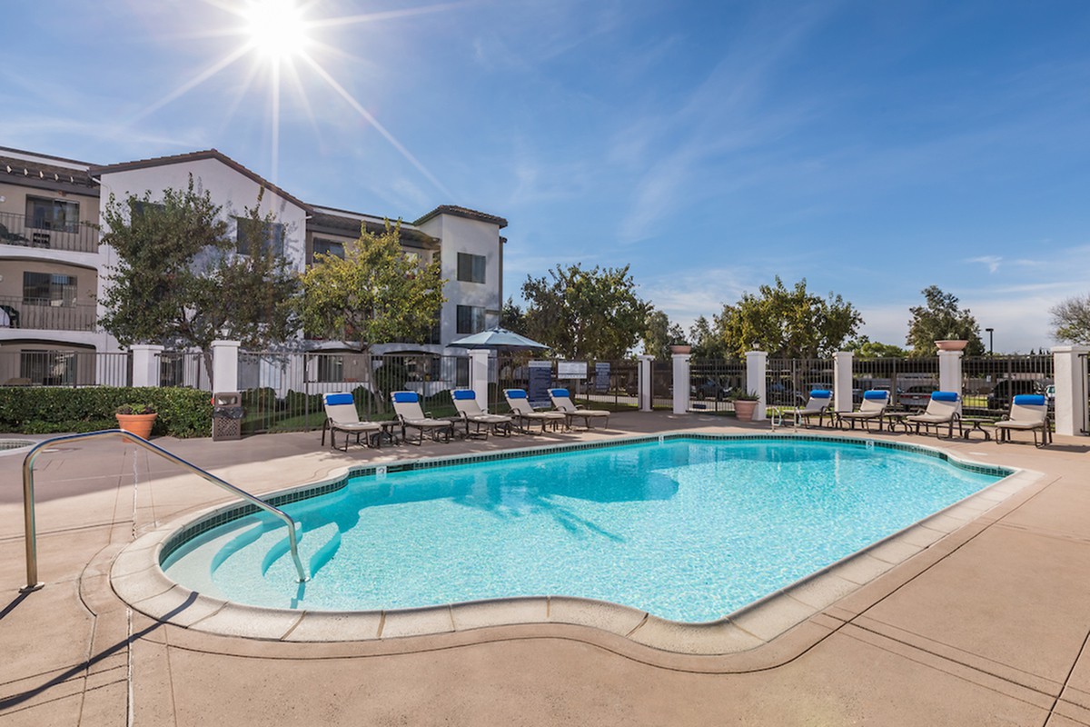 A sunny day by the outdoor swimming pool with deck chairs in front of a residential building.