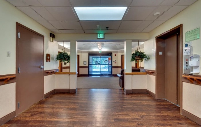 A well-lit hallway with wooden floors and an exit sign above the door.