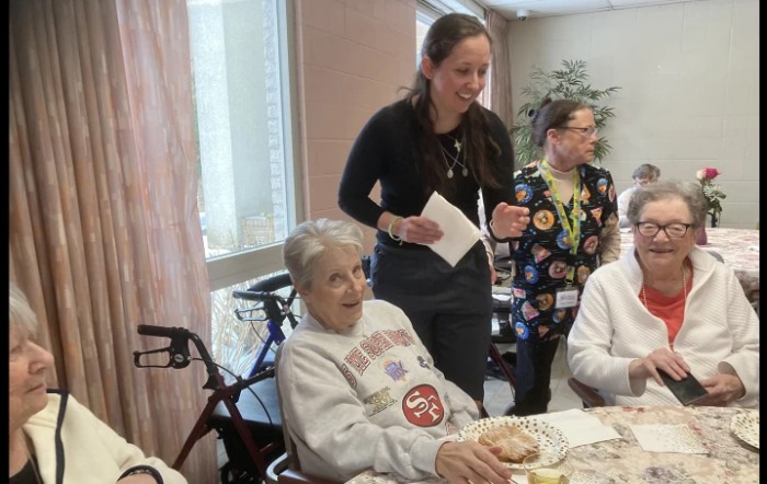 A group of people gathered around a dining table in a care home setting.