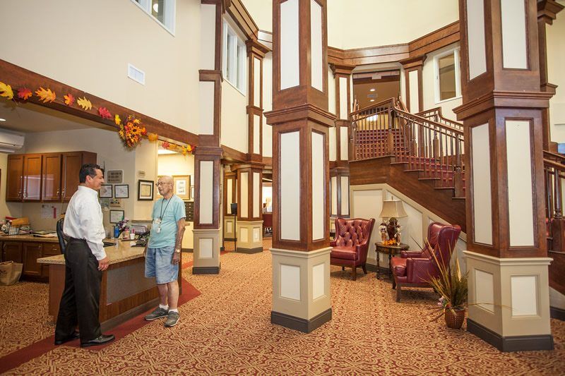 A hotel lobby with a reception desk and guests interacting, featuring elegant interior design and a staircase in the background.