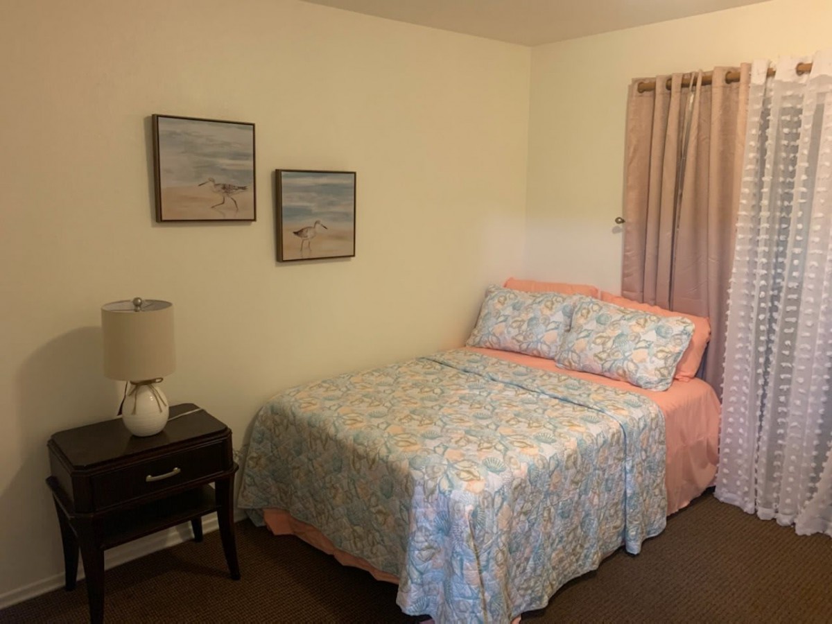 A cozy bedroom with a neatly made bed, decorative artwork, and a nightstand with a lamp.