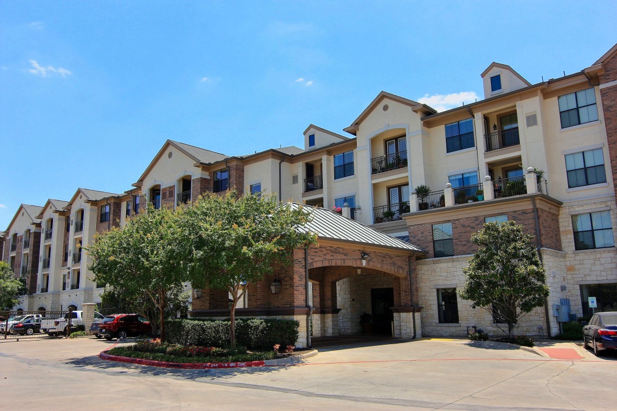 Exterior view of a multi-story residential building with trees and a clear sky.