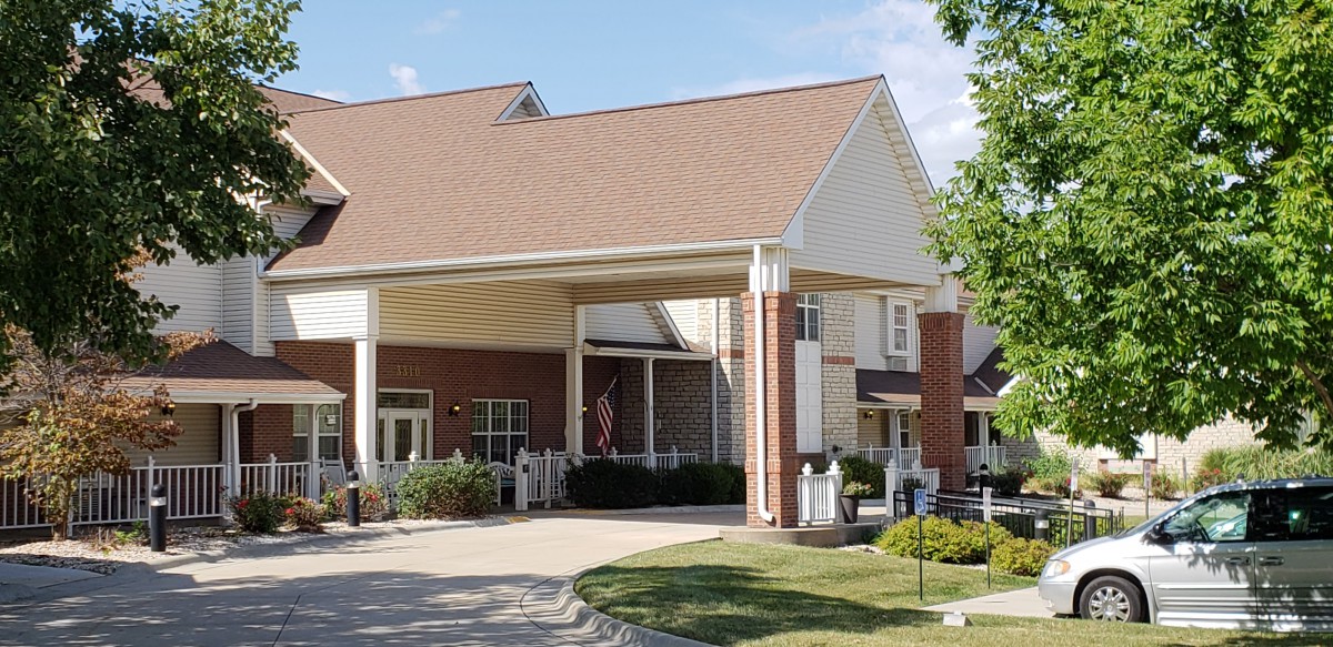 A well-maintained building entrance with columns, surrounded by greenery under a clear sky.