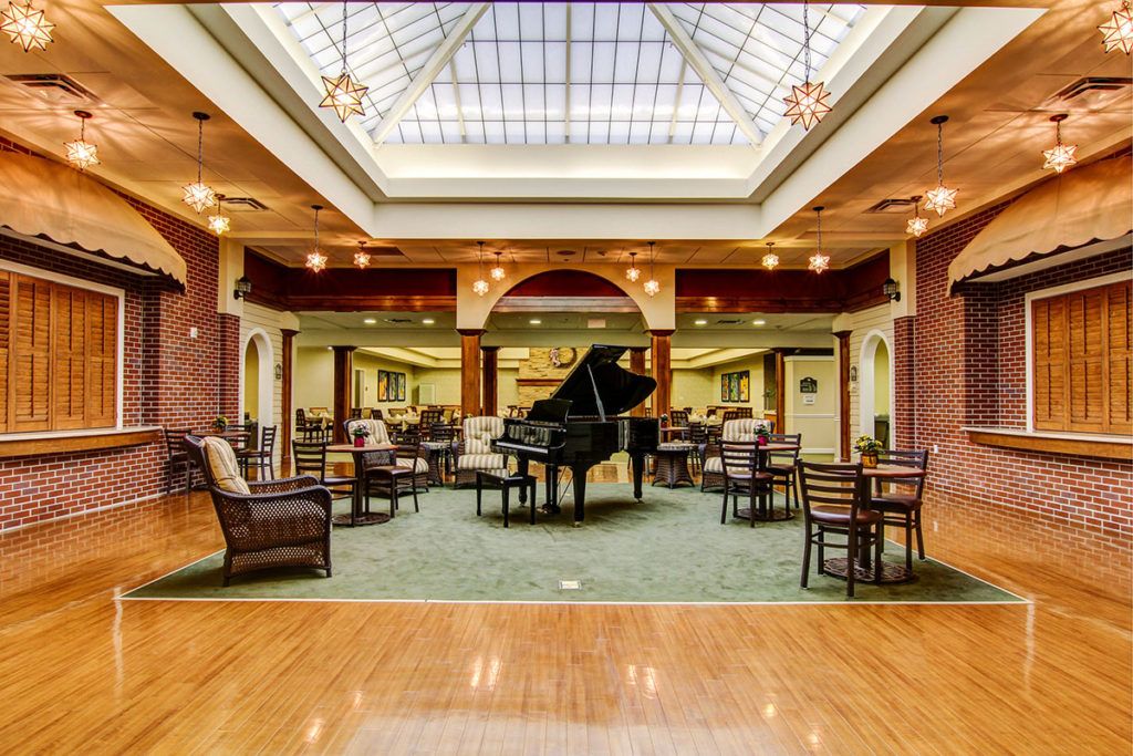 A luxurious lounge area featuring a grand piano, surrounded by comfortable seating and illuminated by an ornate skylight.