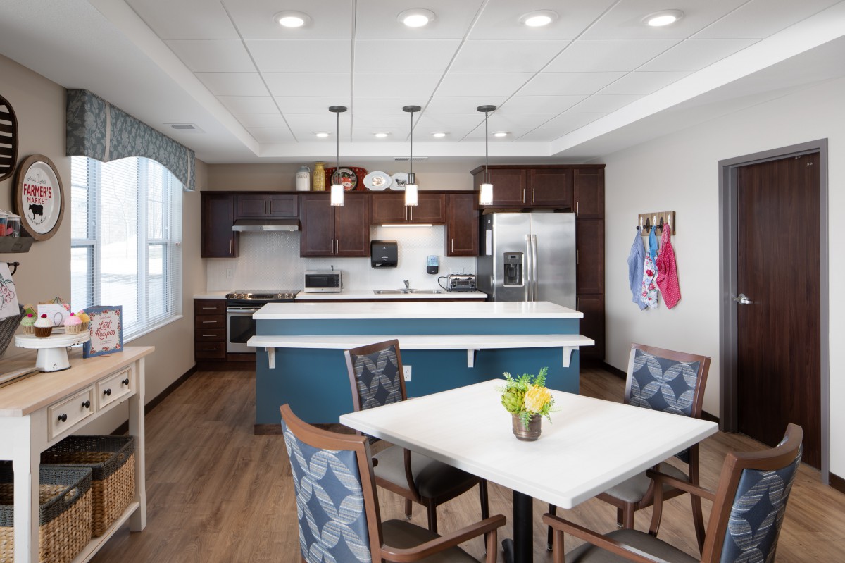 A modern kitchen with a central island and dining area, featuring pendant lighting and stainless steel appliances.