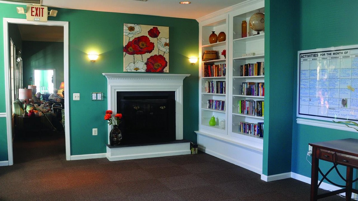 A cozy living room with a fireplace, built-in bookshelf, and green walls adorned with floral artwork.