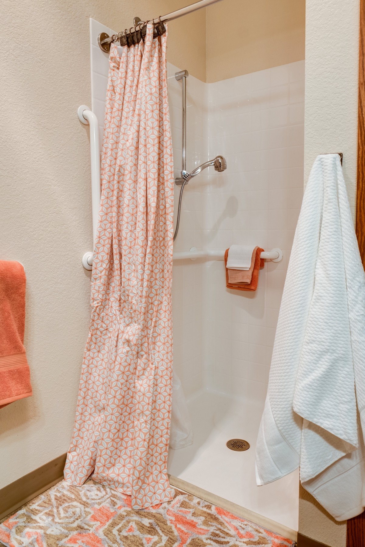 A bathroom featuring a shower with a floral curtain and various towels on display.