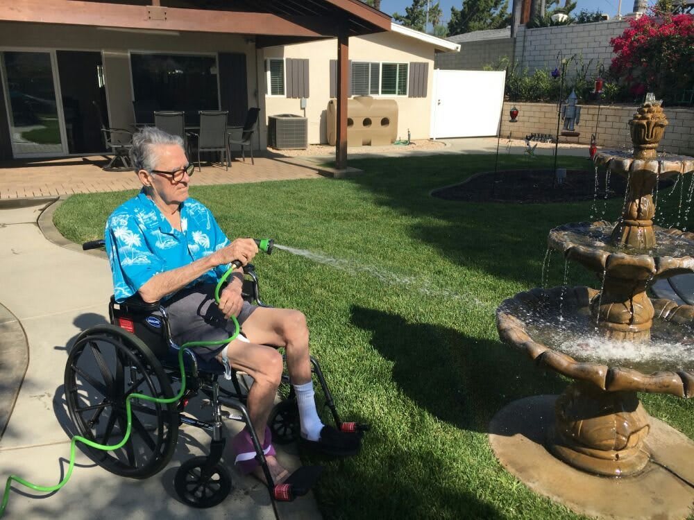 A person in a wheelchair watering a garden fountain on a sunny day.