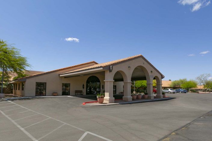 A commercial building with arched entrances and a parking area, under a clear blue sky.