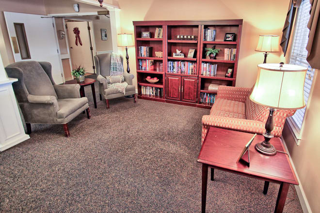 A cozy living room with bookshelves, comfortable chairs, a sofa, and warm lighting.
