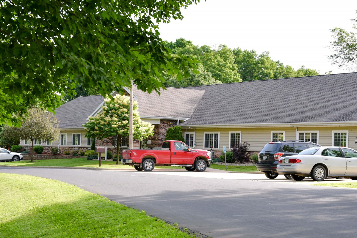 A suburban residential house with parked cars on the driveway surrounded by trees.