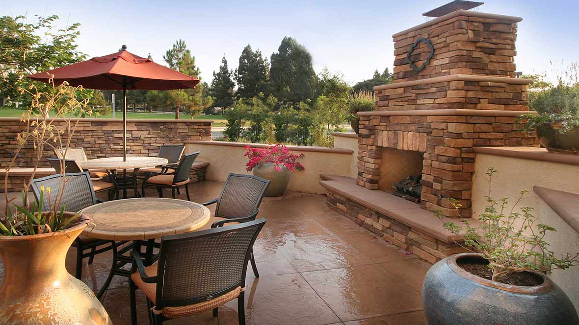 A cozy patio with outdoor seating and a stone fireplace, offering a relaxing garden view.