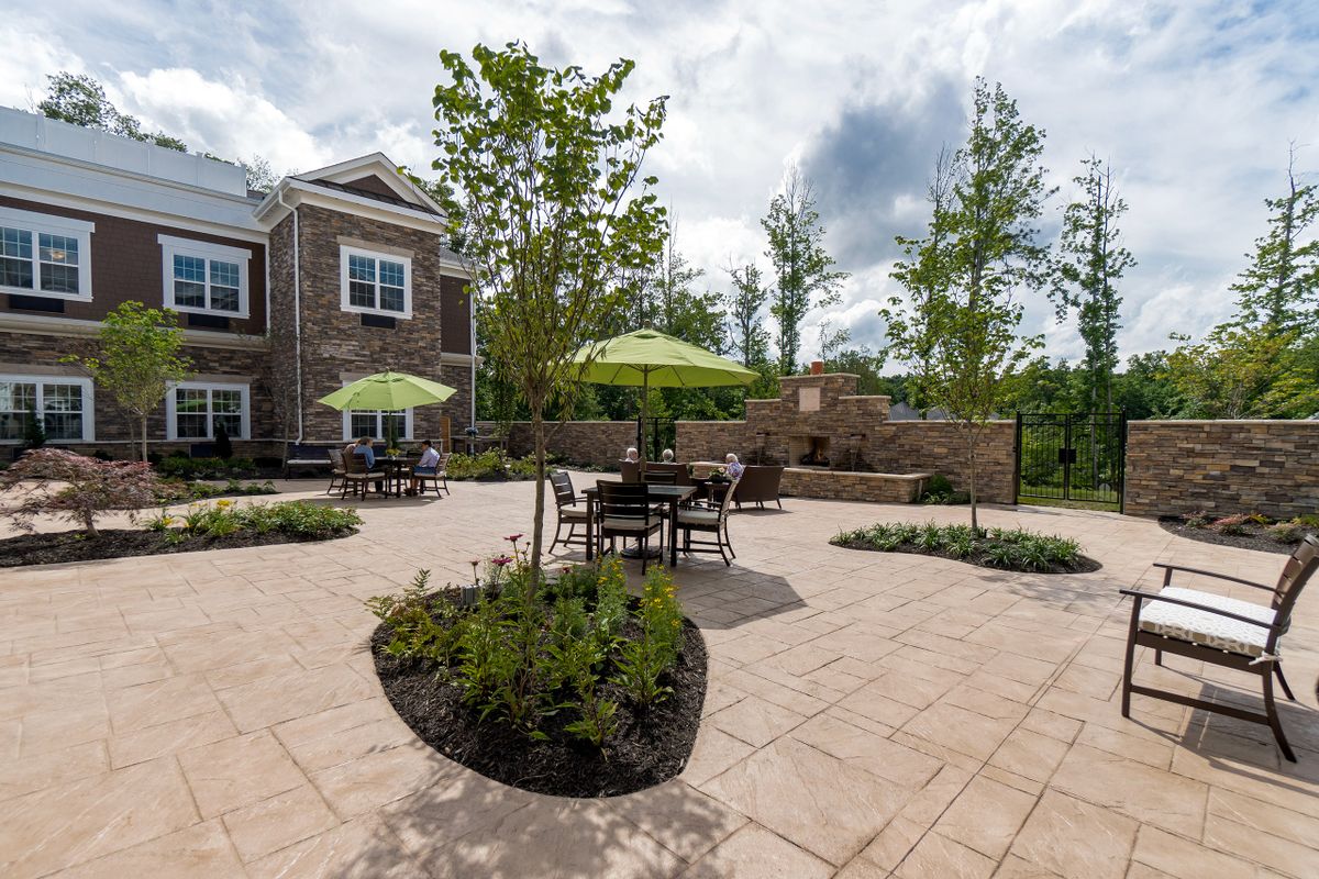 A well-landscaped outdoor patio area with tables, chairs, and umbrellas near a residential building.