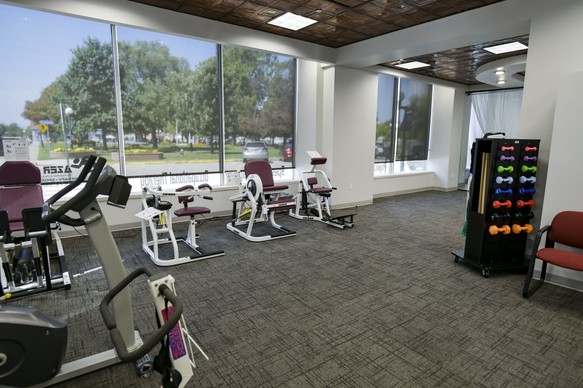 A spacious gym with various exercise machines and large windows overlooking the outdoors.