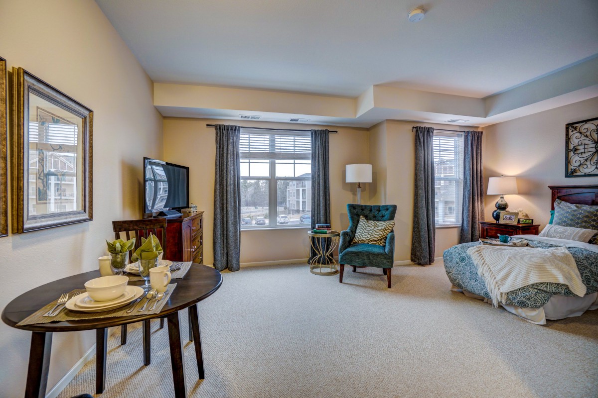 A cozy living room with a television, armchair, and large windows.