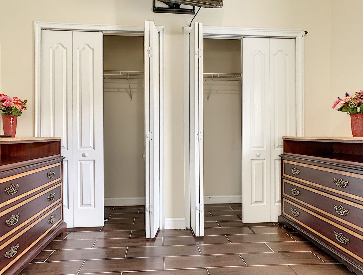An empty bedroom closet with open doors, featuring wooden flooring and dressers on both sides.