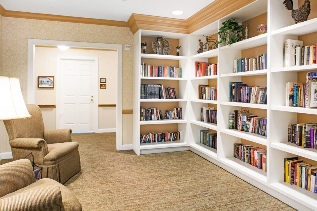A cozy library corner with white shelves filled with books and a comfortable armchair.