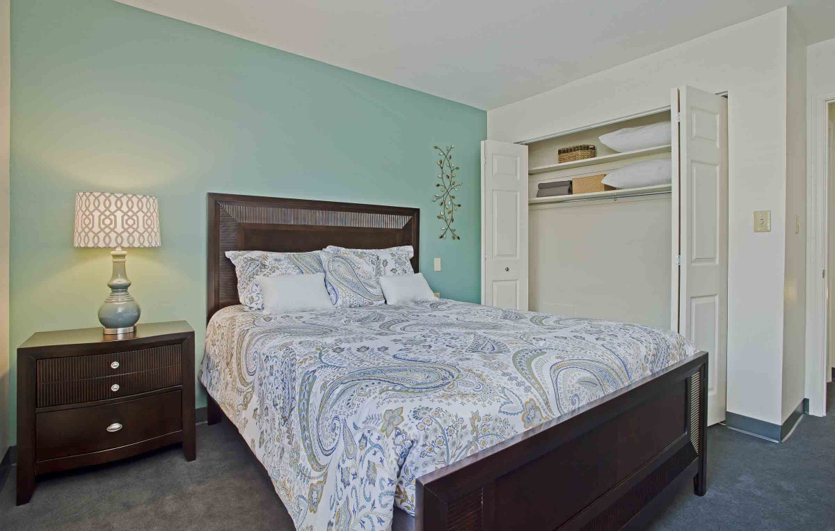 A cozy bedroom with a neatly made bed and an open closet.