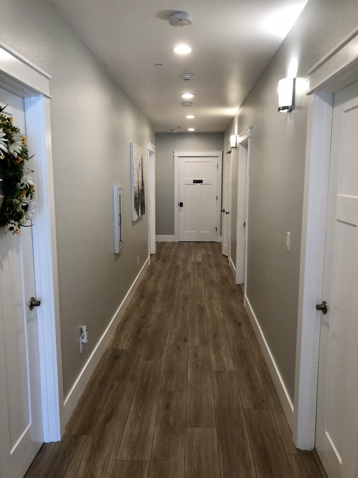 A modern hallway with wood flooring and neutral-colored walls, featuring multiple doors and stylish lighting.