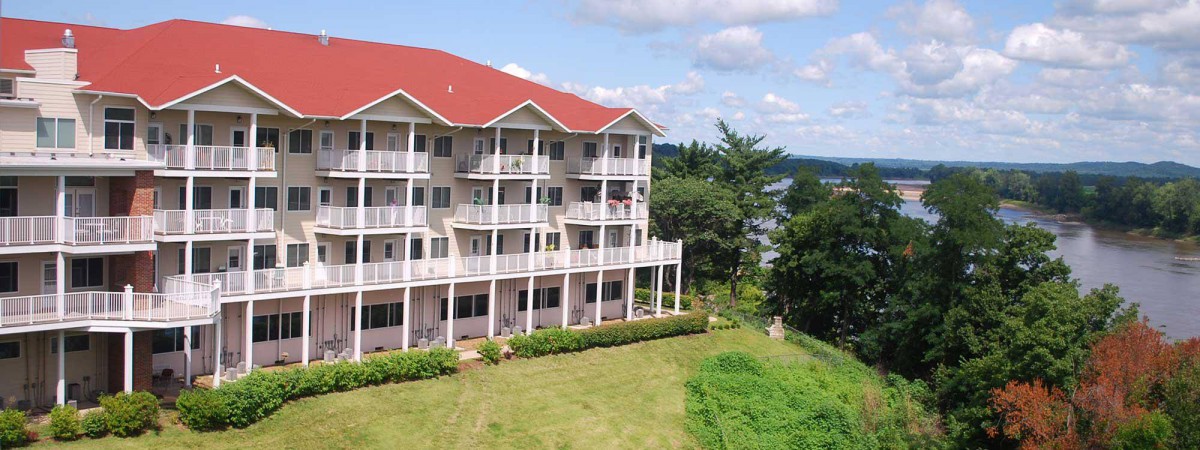 A multi-story apartment building with balconies surrounded by greenery and a clear sky.