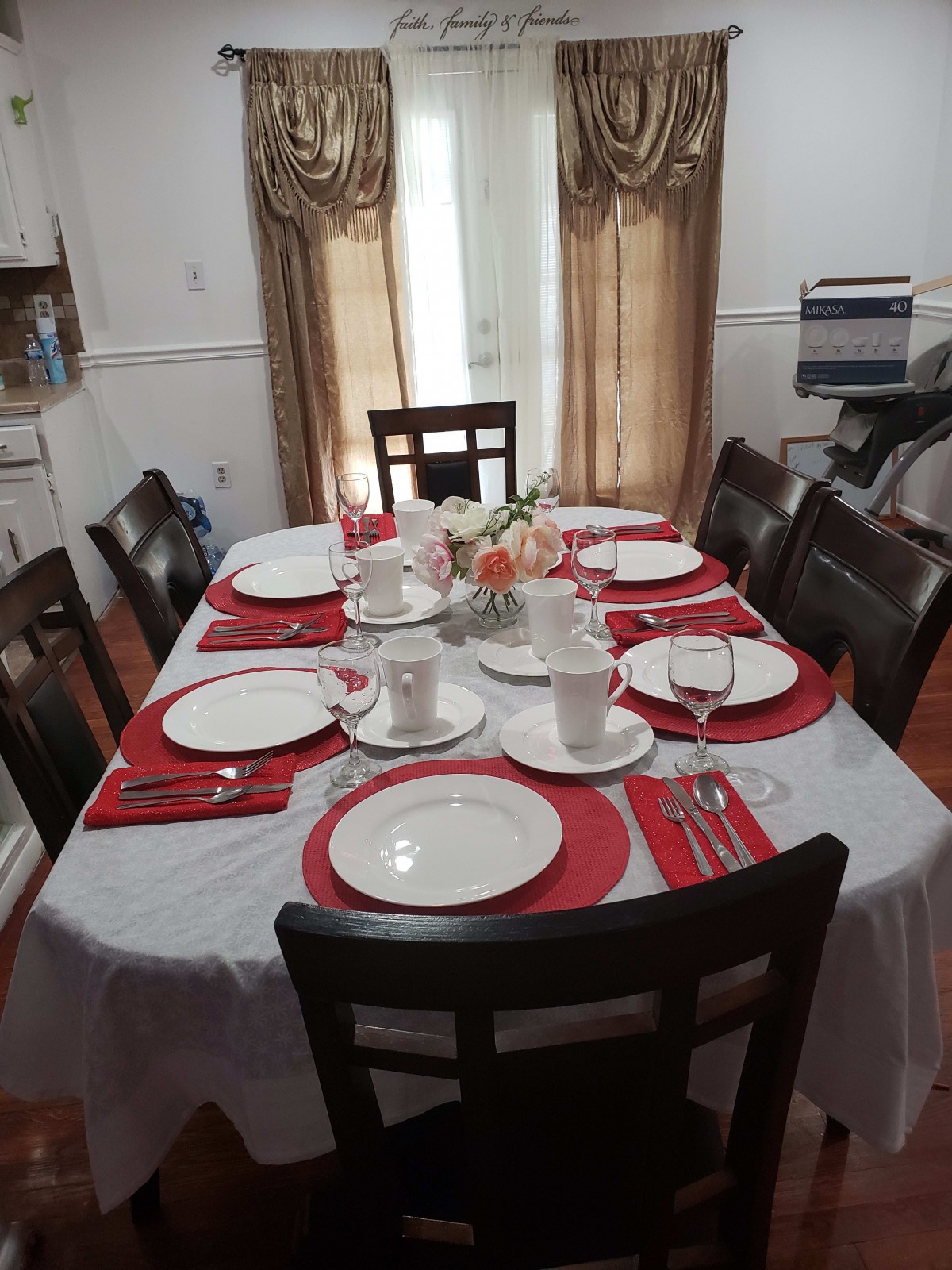 A dining table set for six with white plates and red placemats.