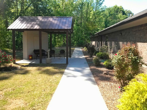 A serene pathway leading through a landscaped area, showcasing a pavilion and nearby building in a natural setting.