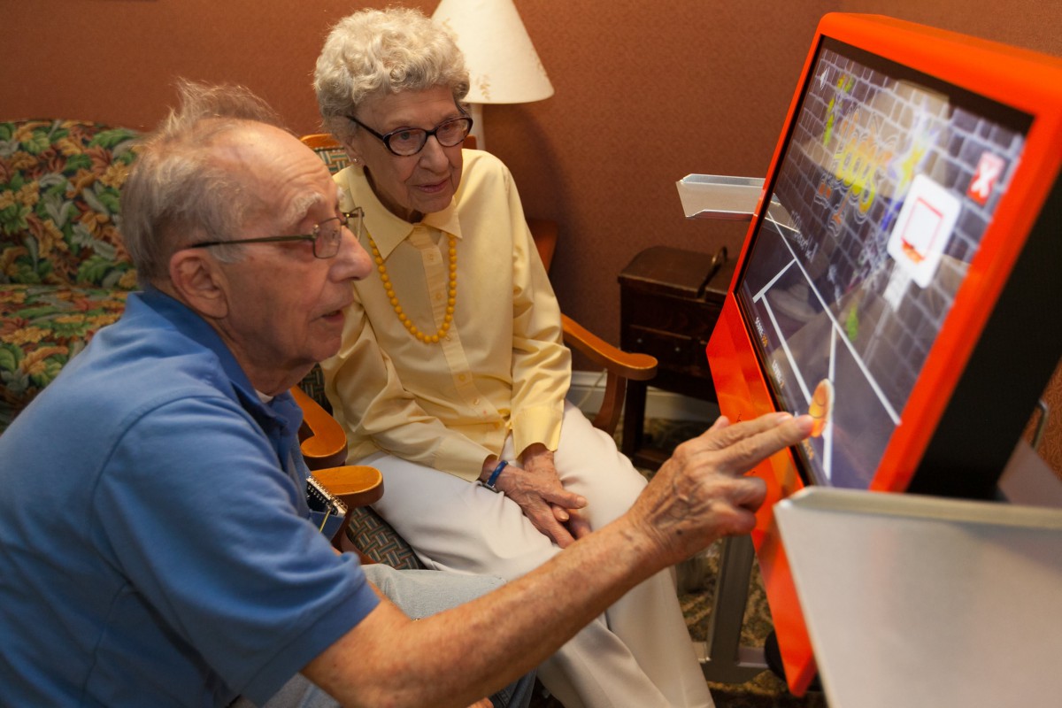 Two elderly individuals engaging with a touchscreen device indoors.