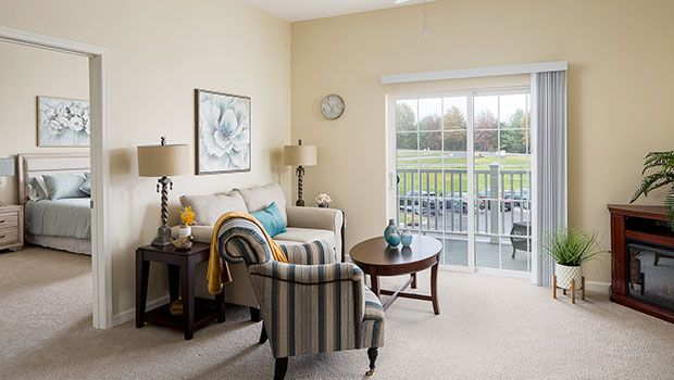A cozy living room with a sofa, armchair, and coffee table, featuring a large balcony door bringing in natural light.