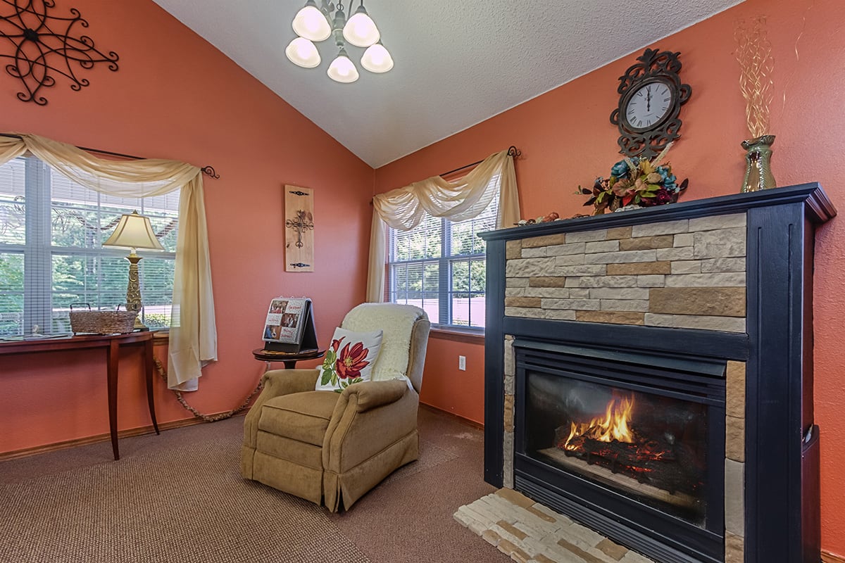 A cozy living room with an armchair beside a stone-faced fireplace and an orange accent wall.