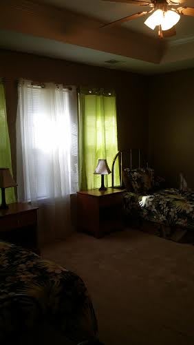A cozy bedroom with twin beds, nightstands, and green curtains.