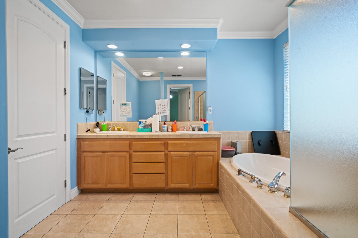 A spacious bathroom with blue walls, featuring a large mirror above a wooden vanity and a bathtub to the side.