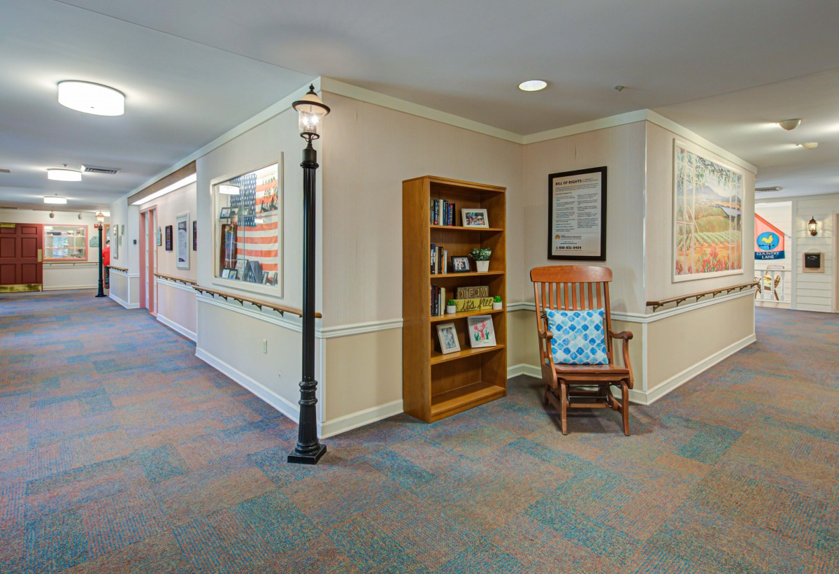 A cozy hallway featuring a bookshelf and a rocking chair next to a decorative lamp post.