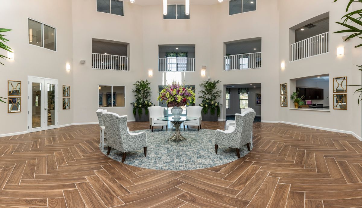 A modern lobby with a circular seating area featuring chairs around a table, adorned with plants and natural light.
