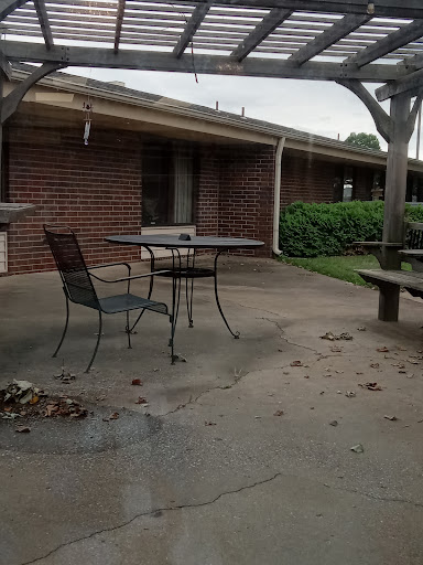 A quiet outdoor patio area with a table and chairs, surrounded by a brick building and greenery.
