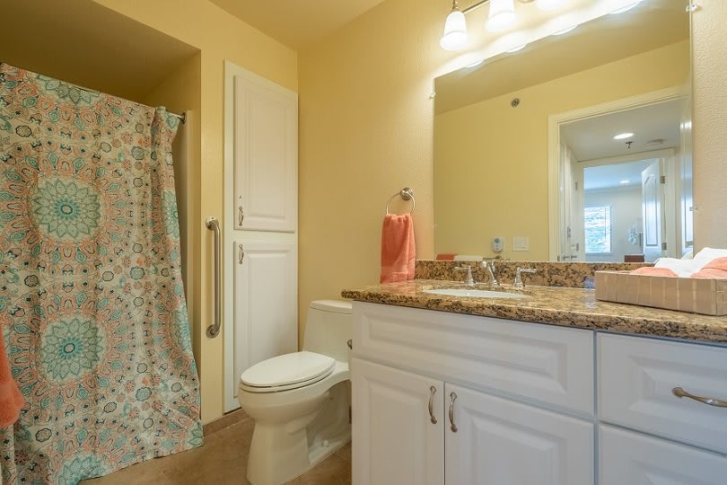 A well-lit bathroom with a shower, toilet, sink, and storage cabinets.